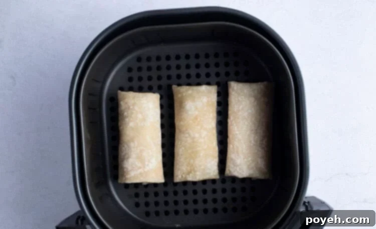 Frozen burritos arranged neatly in a single layer within an air fryer basket, ready for cooking.