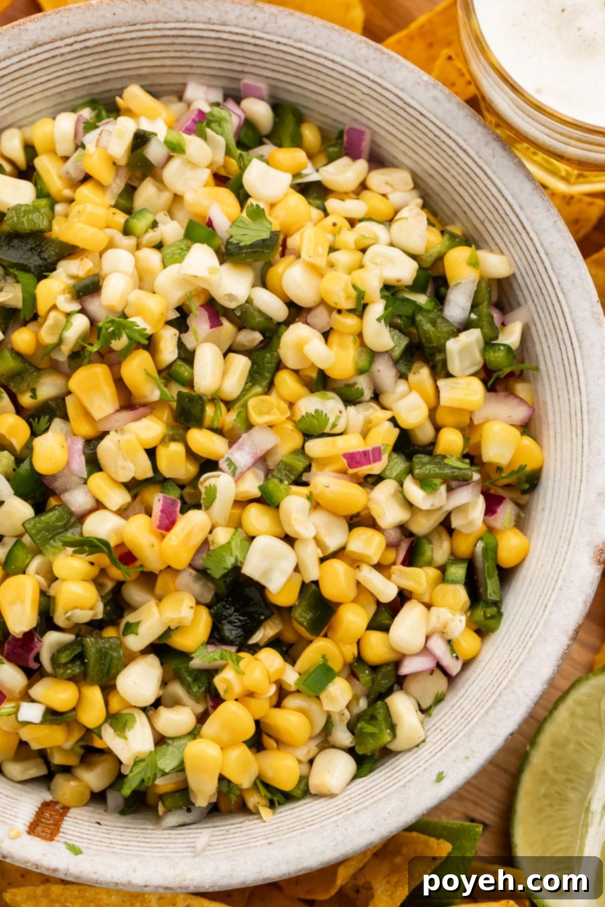 Overhead view of a white bowl of homemade roasted chili corn salsa on a rustic wooden table, garnished with fresh cilantro.