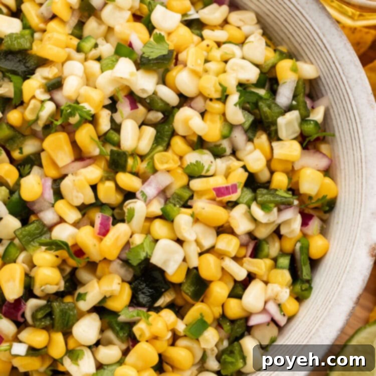 Overhead view of a white bowl of roasted chili corn salsa on a table.
