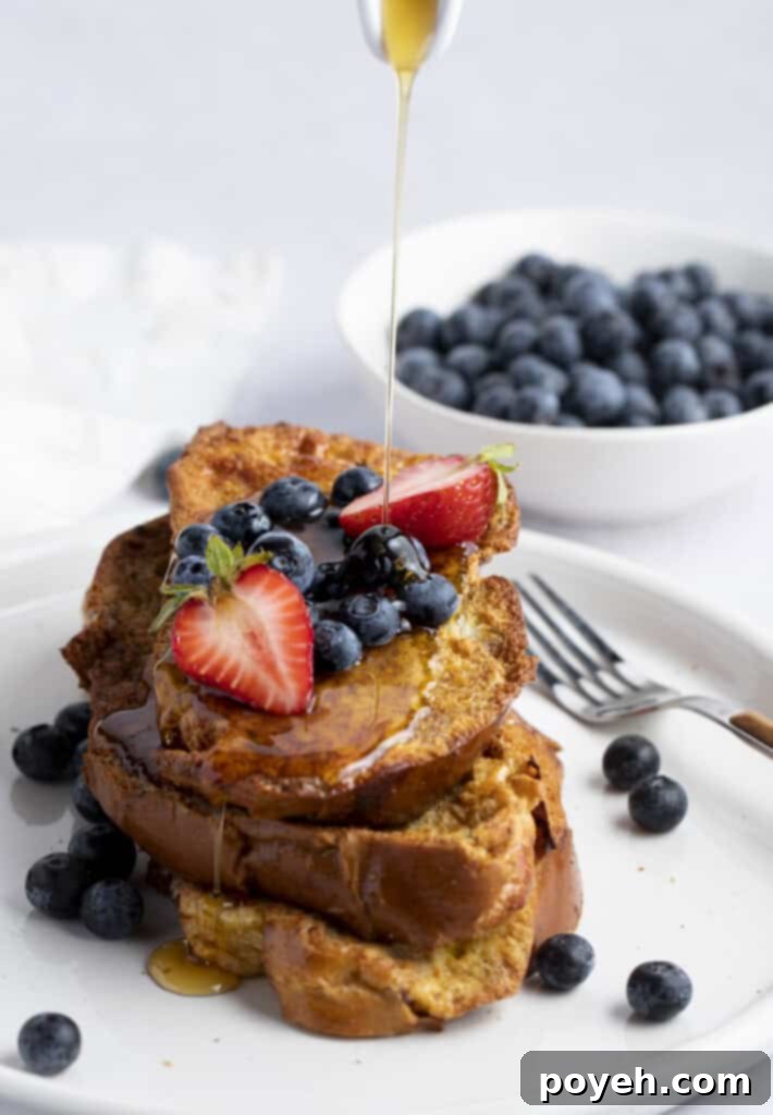 Syrup poured over air fryer french toast on a plate topped with blueberries and strawberries