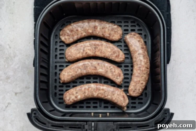 Step-by-step image showing uncooked brats carefully arranged in a single layer within an air fryer basket.