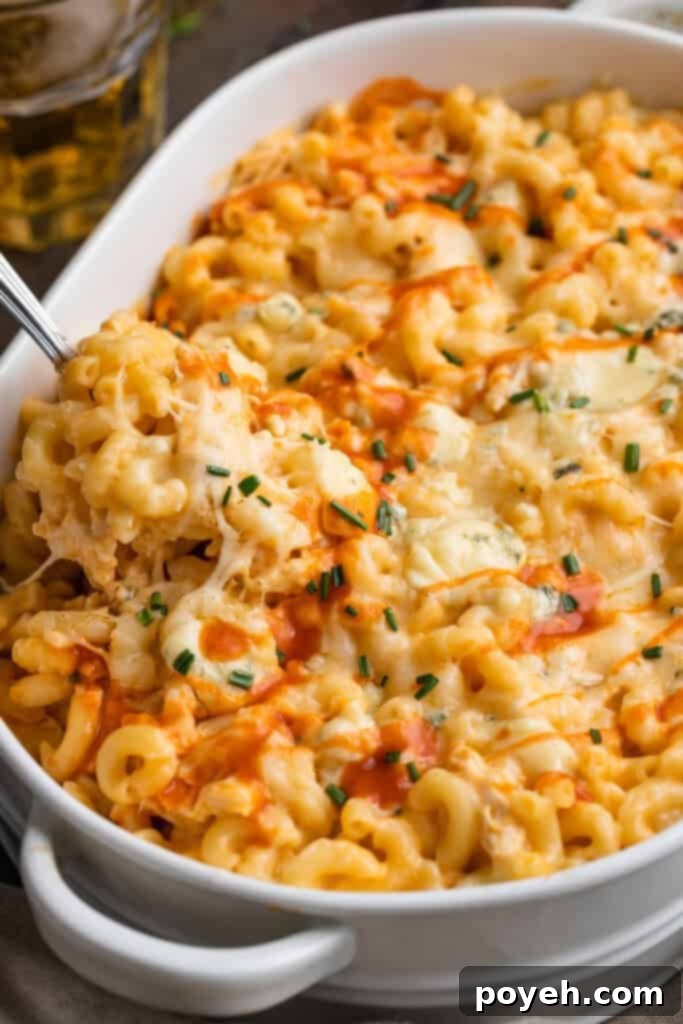 Angled view of a spoonful of buffalo chicken mac and cheese resting on a casserole dish of mac and cheese, showcasing its creamy texture and golden-brown top.