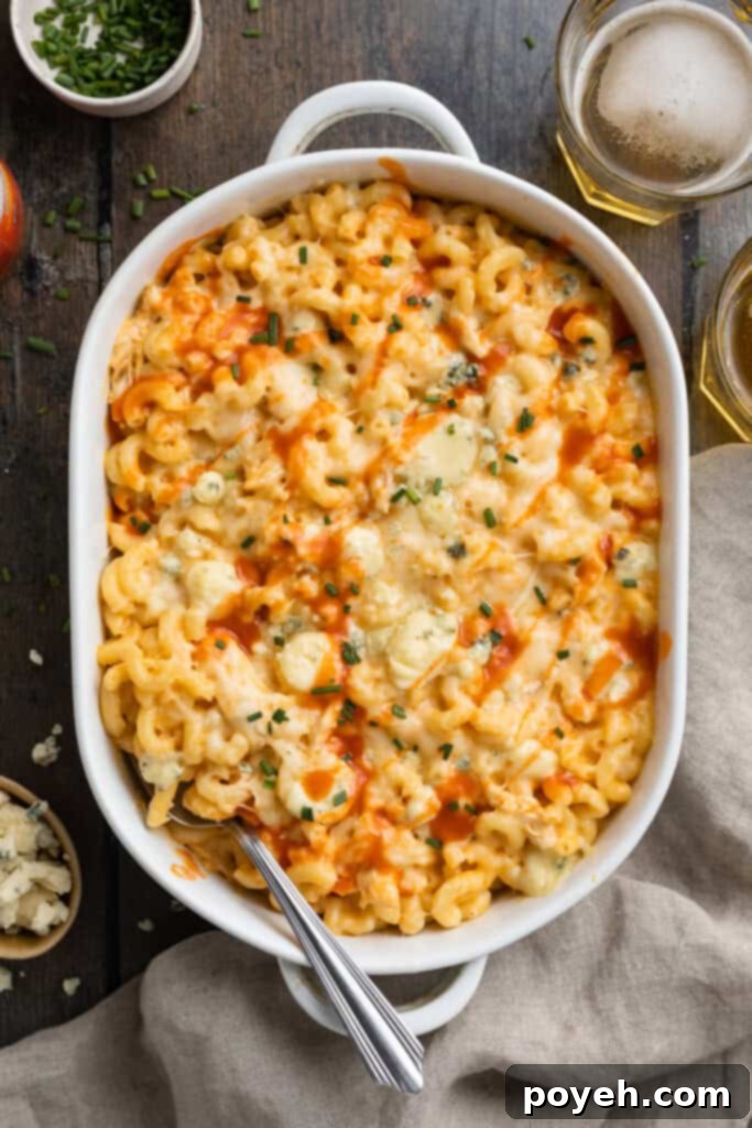 Overhead view of buffalo chicken mac and cheese in a casserole dish with a serving spoon on a dark wooden background, highlighting its rich color and inviting texture.