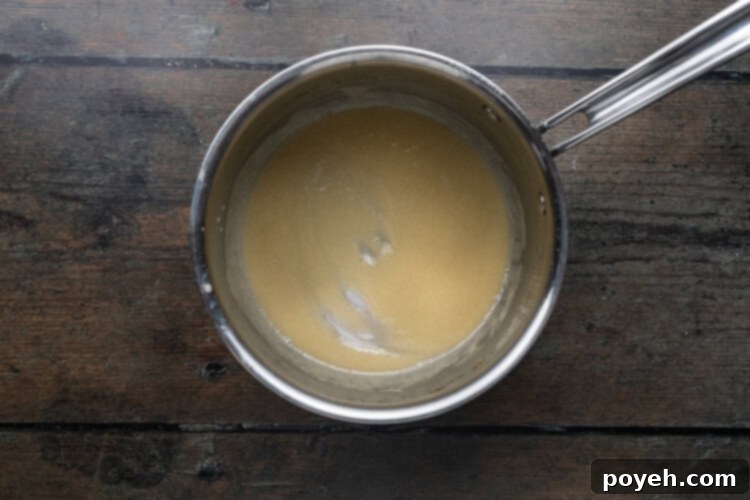 Overhead view of a silver pot of melted butter on a dark wooden background.
