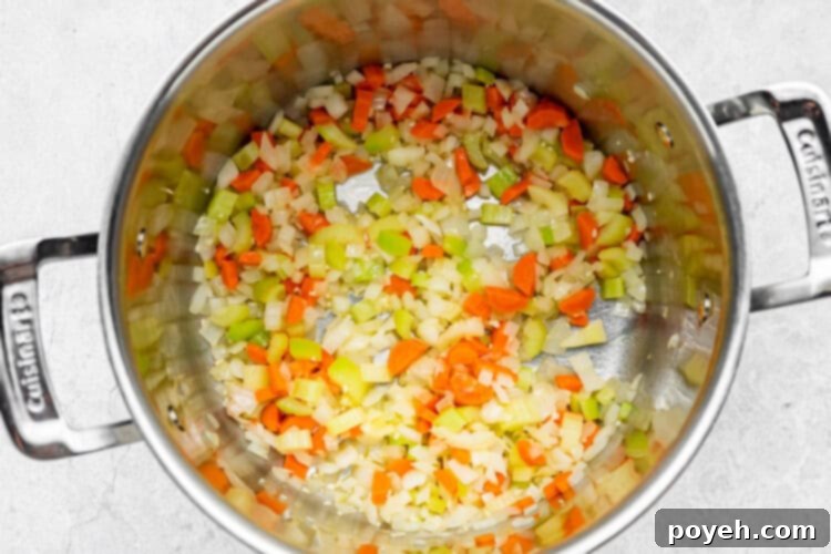 Sautéing the mirepoix (onion, carrots, celery) and garlic in melted butter in a large pot, the vegetables softening and releasing their aromas, marking the first step of building the soup's flavor.