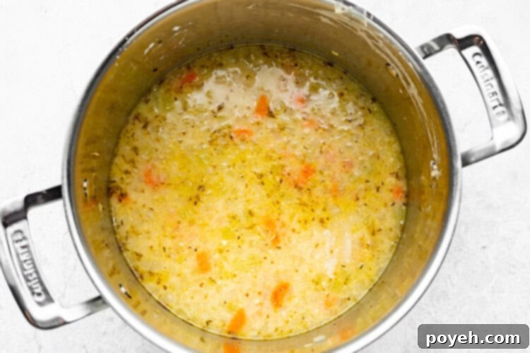 The soup base, having just been brought to a boil and now simmering, thickening to a rich, creamy consistency as the chicken broth and half and half blend with the roux and vegetables.