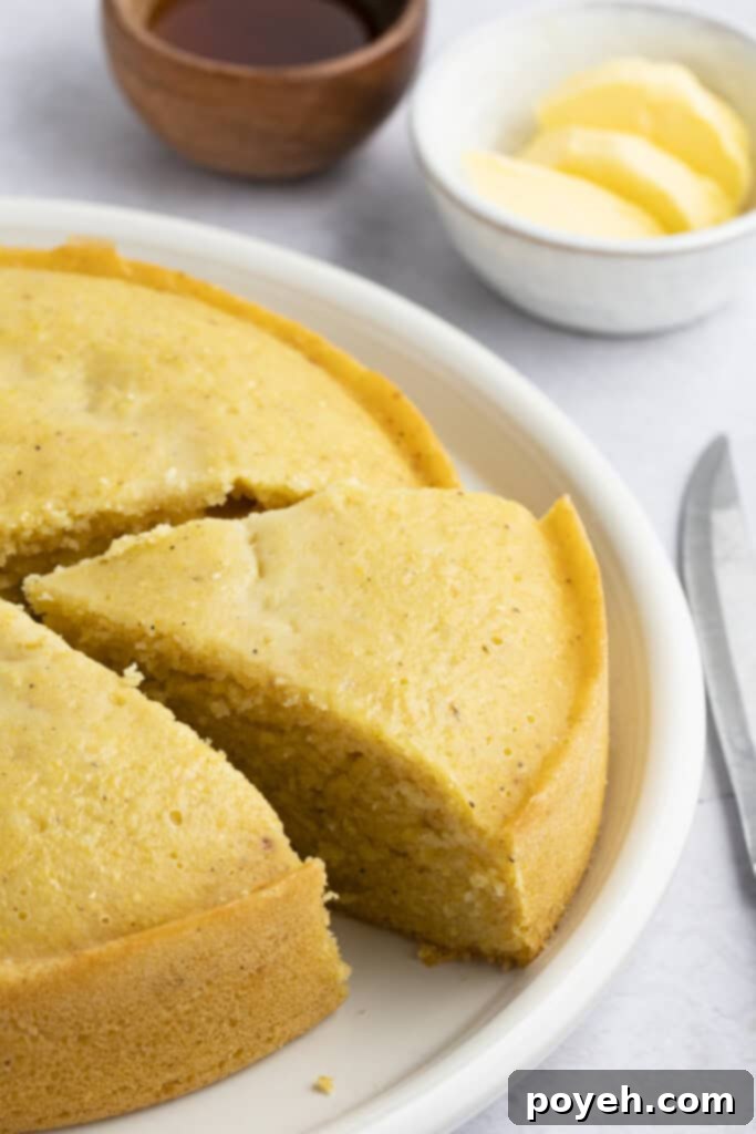 A beautifully baked Instant Pot cornbread, with one wedge already cut, resting on a white plate