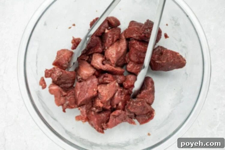 Cubed beef chuck seasoned with salt and pepper in a mixing bowl.