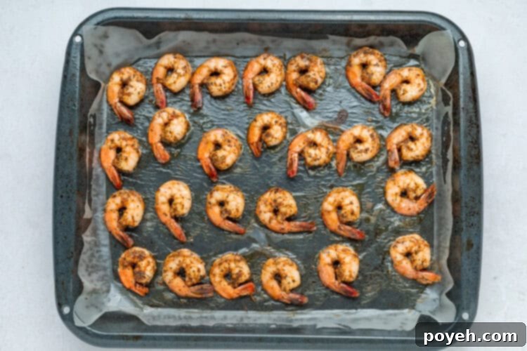 Buffalo shrimp cooking on a baking sheet under the broiler.