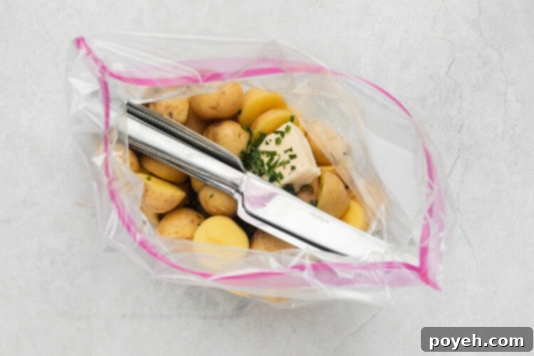 Sliced baby potatoes, butter, salt, and fresh herbs placed inside a zip-top bag with heavy utensils, ready for sealing.