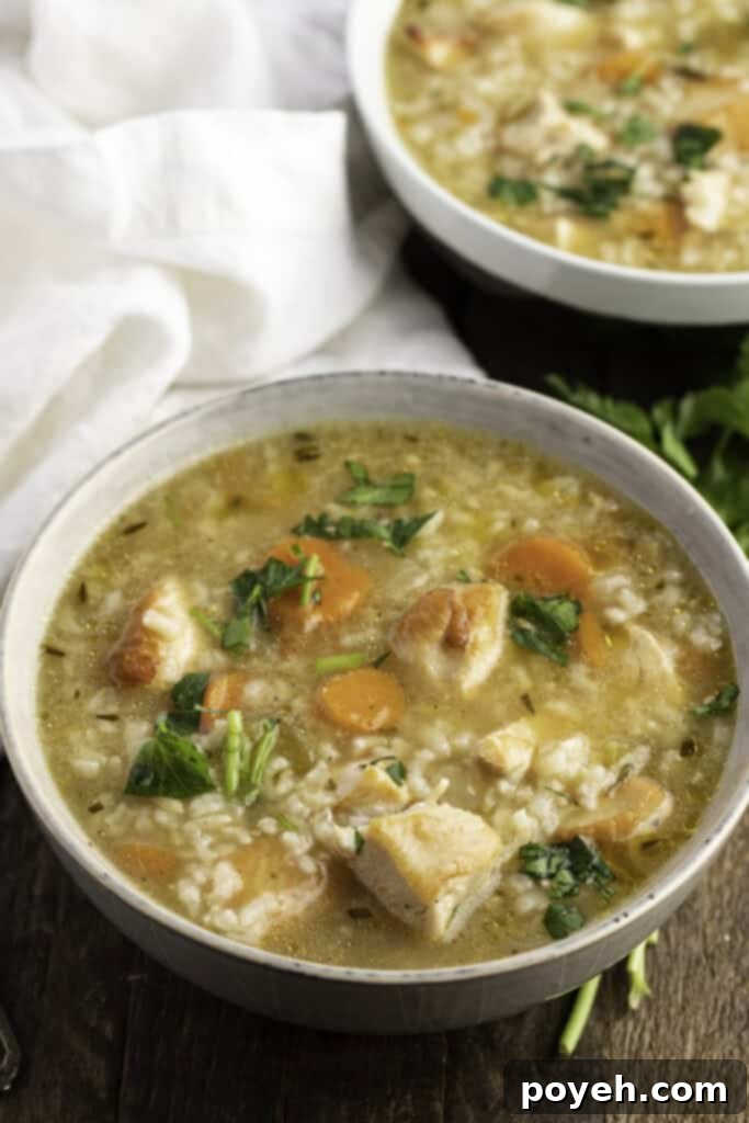 3/4-angle view of two bowls of Instant Pot chicken and rice soup on a wooden table, with fresh bread nearby.