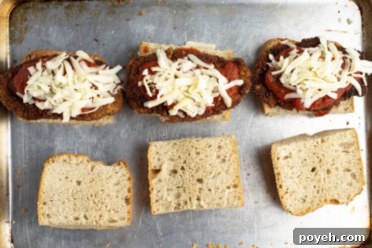 Assembled chicken parm sandwiches on a baking sheet, ready for final melting.