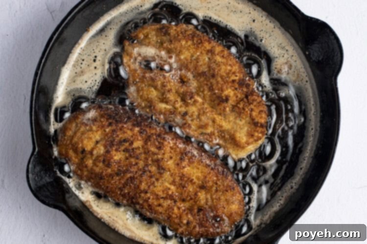 Pan-fried breaded chicken cutlets sizzling in a cast iron skillet.