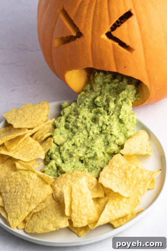 Angled view of a puking pumpkin with guacamole on a plate surrounded by tortilla chips for a Halloween party