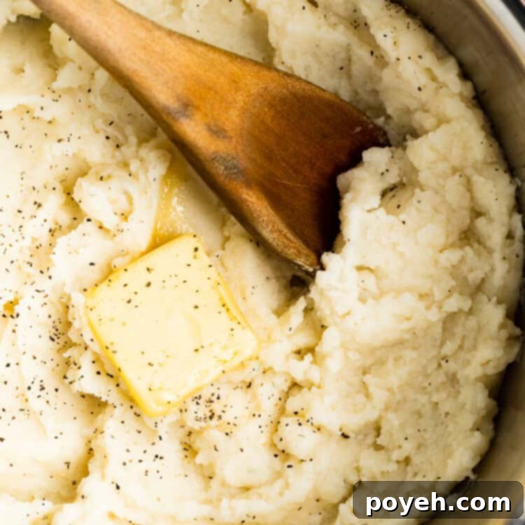overhead image of mashed potatoes in a pot with butter and a wooden spoon