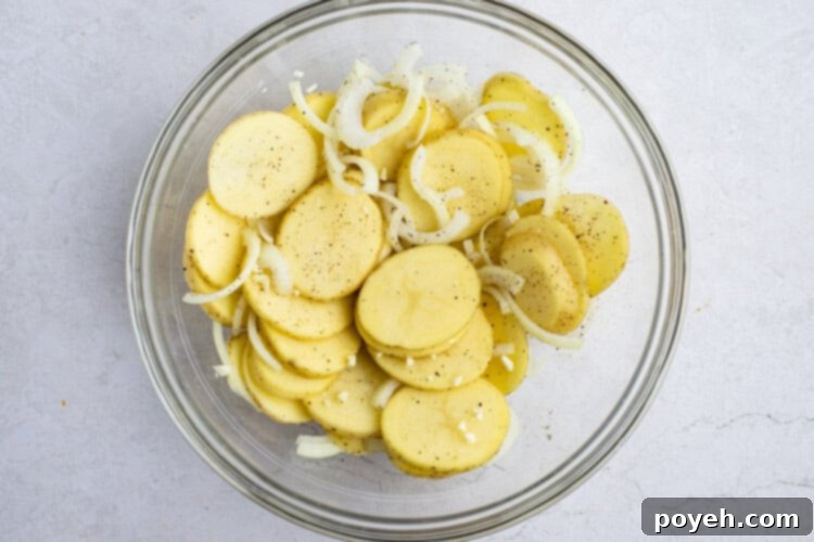 Sliced potatoes and onions seasoned in a glass bowl.