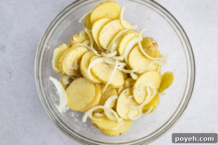 Floured potatoes and onions in a large glass bowl, ready for cooking.
