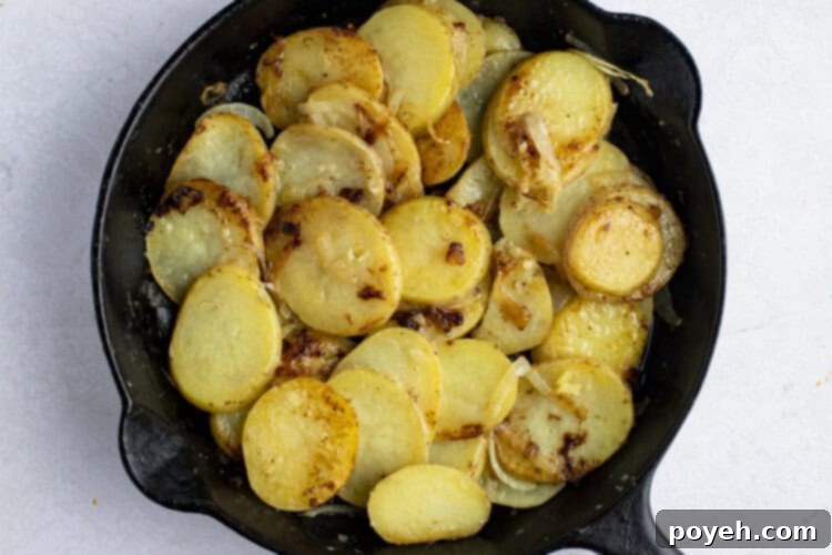 Smothered potatoes simmering in a cast iron skillet with broth, covered.