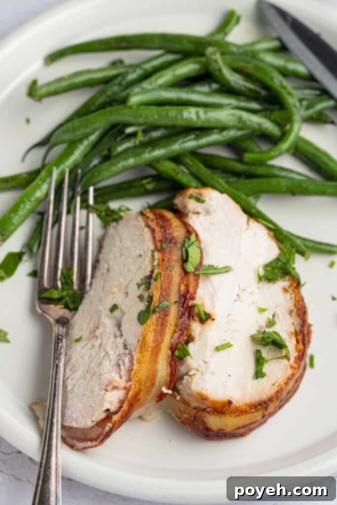 Close-up of perfectly carved slices of Bacon Wrapped Turkey Breast on a plate, garnished with fresh green beans and a fork, ready to be served.
