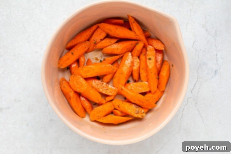 Sliced carrots in a large bowl, seasoned and ready for the air fryer.