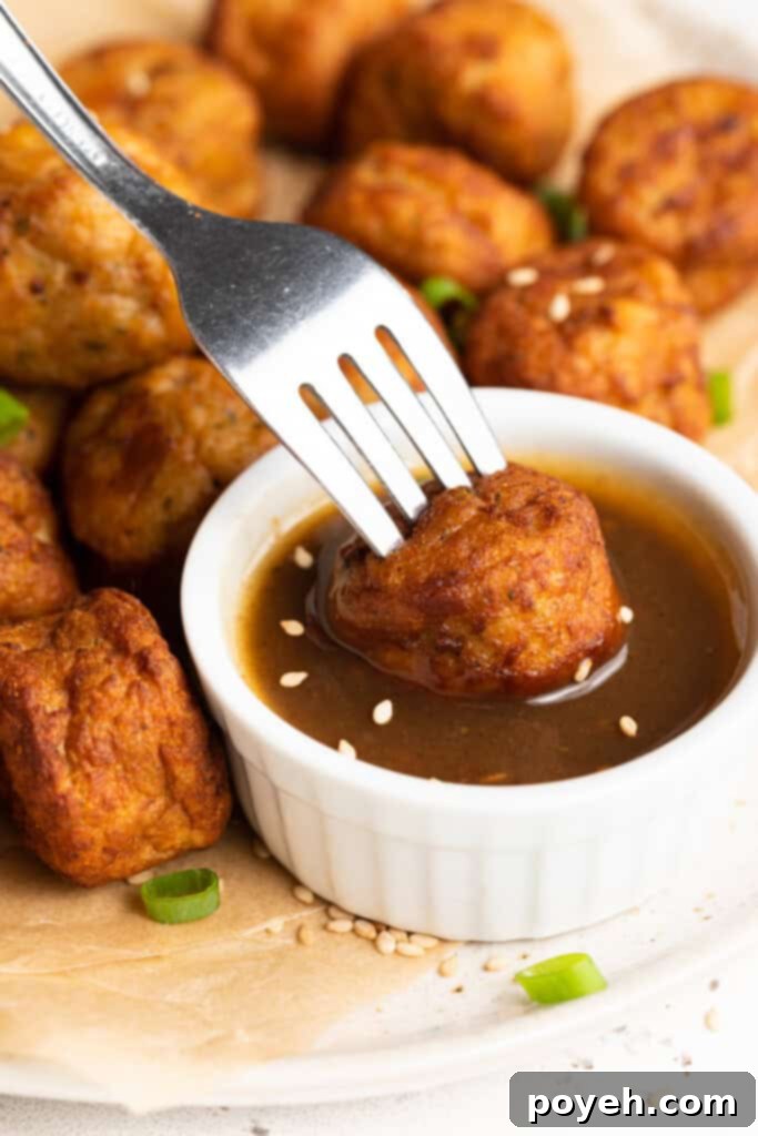Frozen meatballs in air fryer being dipped in teriyaki sauce, illustrating a quick and delicious appetizer.
