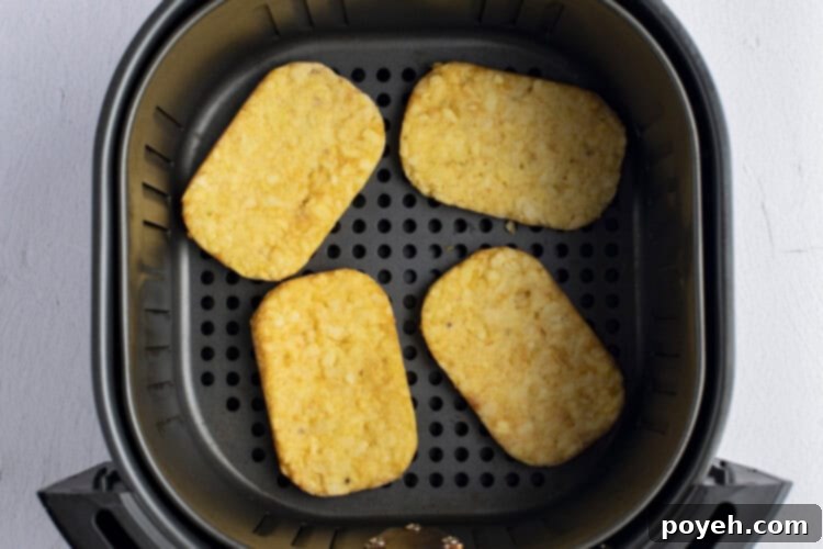 Frozen hashbrowns being placed into an air fryer basket in a single layer