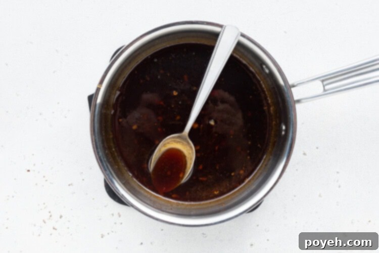 Thickening keto teriyaki sauce in a saucepan, being vigorously whisked after the addition of xanthan gum to achieve a smooth, glossy consistency.