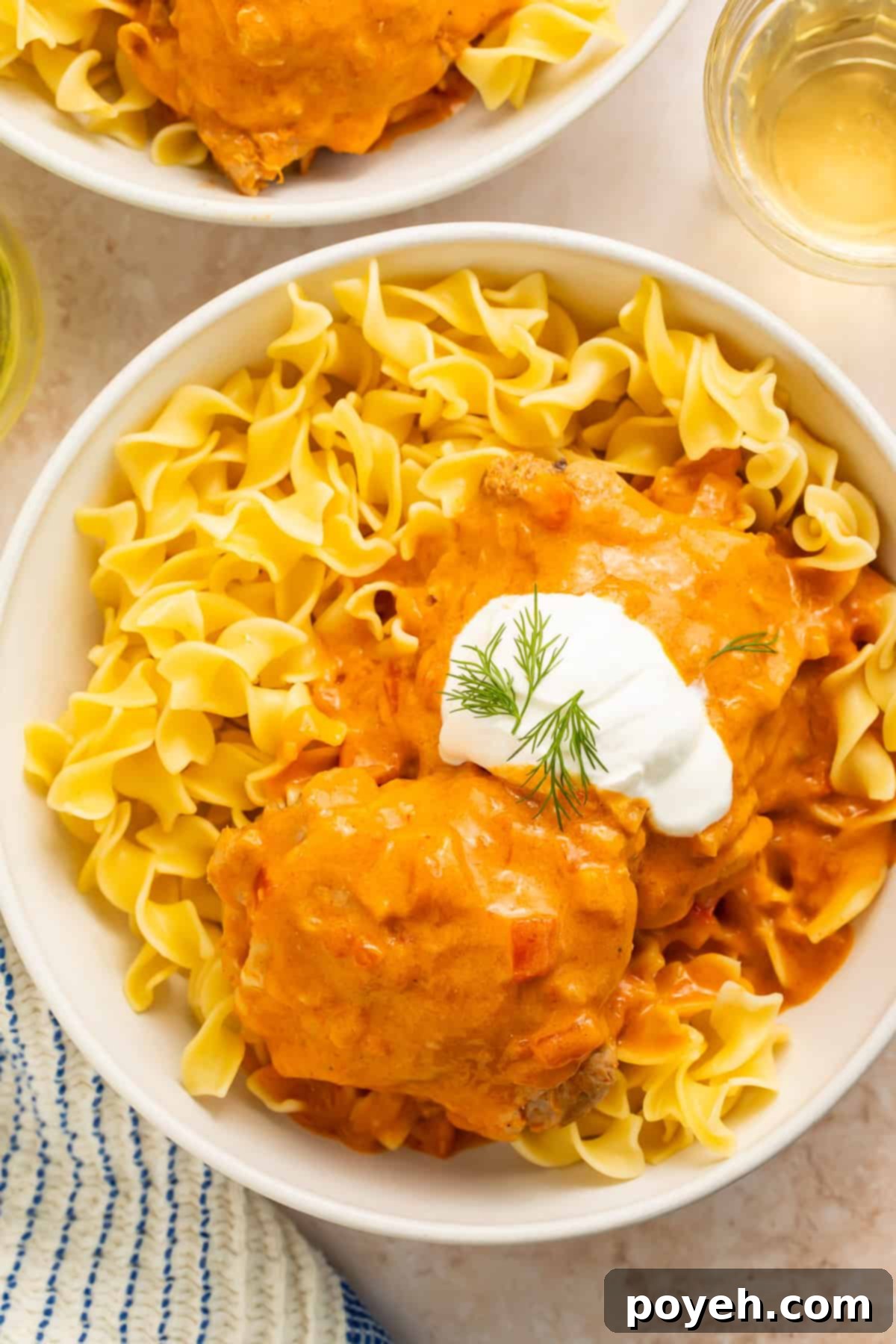 Two bowls of creamy Chicken Paprikash served over egg noodles with a dollop of sour cream and fresh dill garnish.