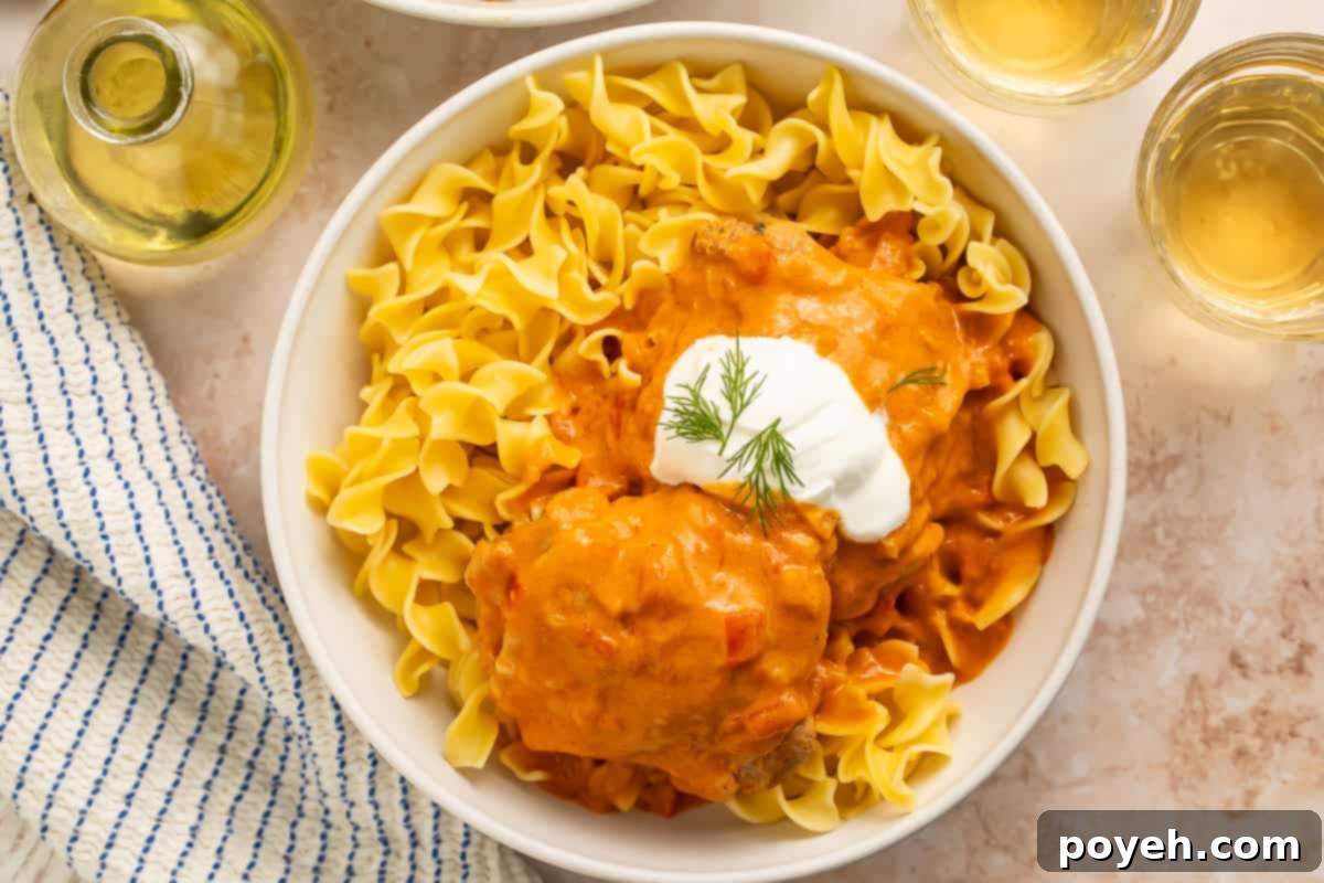A serving of Instant Pot Chicken Paprikash over egg noodles, topped with fresh dill and a generous dollop of sour cream.