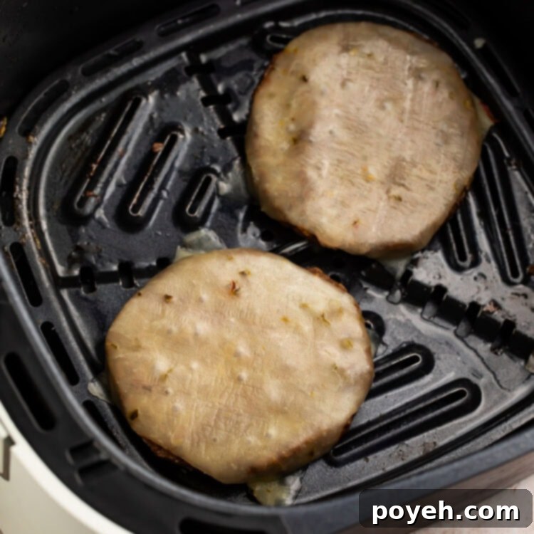 Two perfectly cooked frozen burger patties from the air fryer, topped with melted cheese in an air fryer basket, ready for assembly.