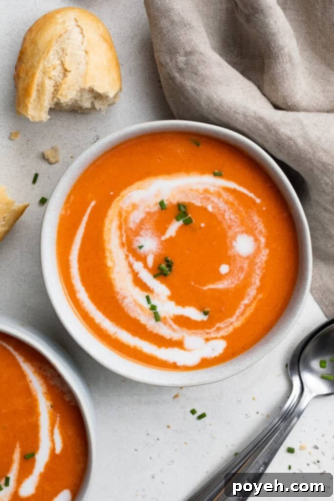 two bowls of gluten free tomato soup with heavy cream swirled on top and bread on the side