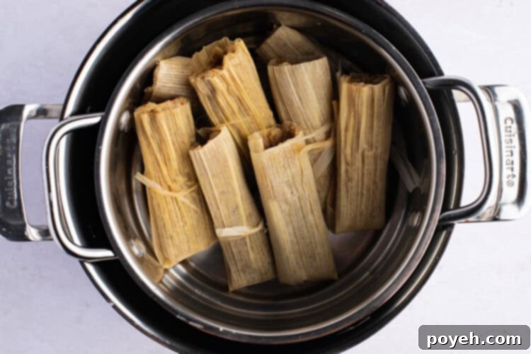 Keto tamales steaming upright in a steamer basket, covered with aluminum foil, on a white background.