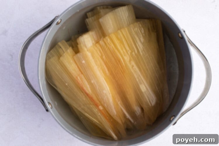 Corn husks soaking in hot water in a large pot, preparing for tamale assembly.