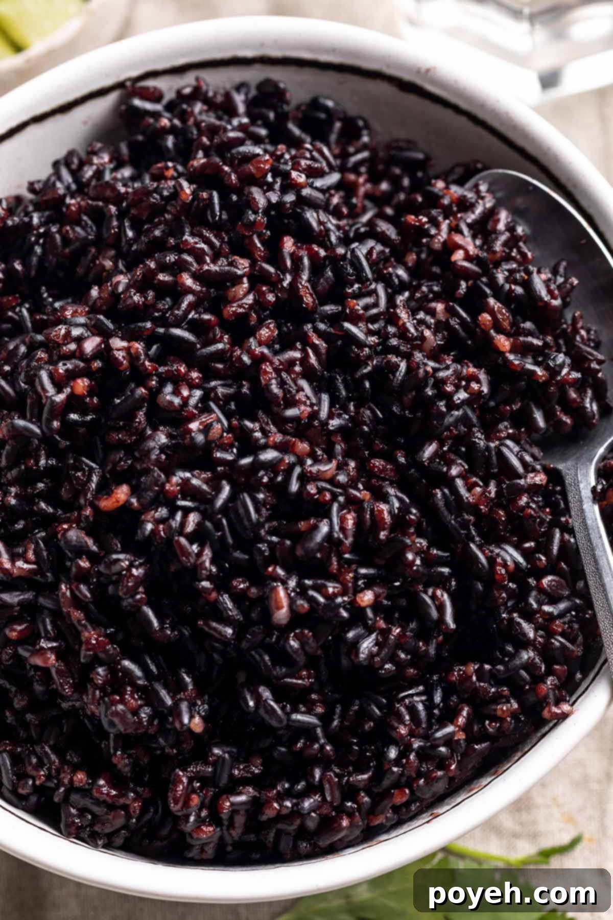 Overhead close-up of tender black rice, cooked in an Instant Pot, served in a large white bowl. A silver spoon rests in the rice.
