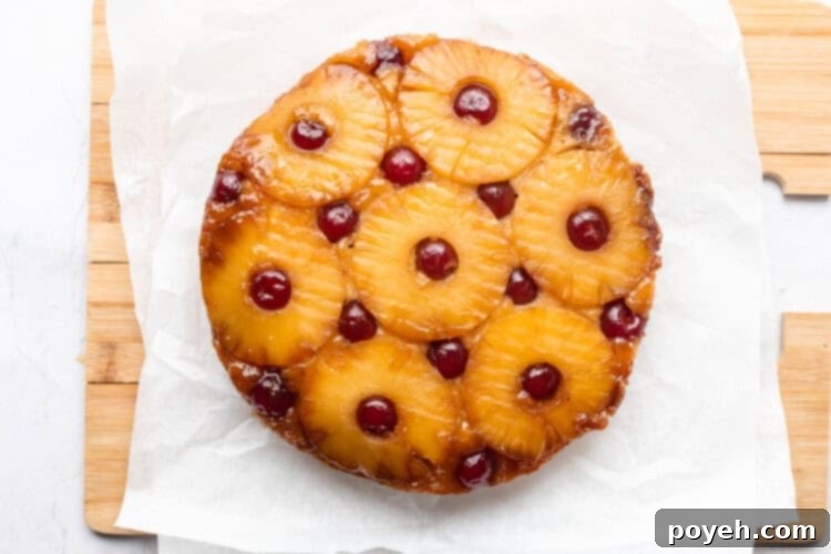 Round vegan pineapple upside down cake cooling on parchment paper on a cutting board, after being inverted.