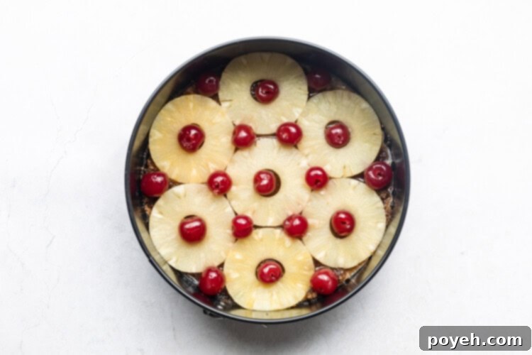Pineapple rings and maraschino cherries arranged in the bottom of a cake pan, ready for the batter.