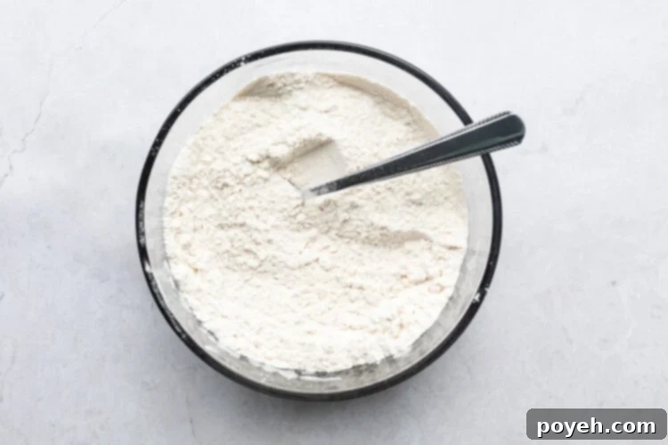 Dry ingredients for vegan pineapple upside down cake, including flour, baking powder, and salt, in a glass mixing bowl.