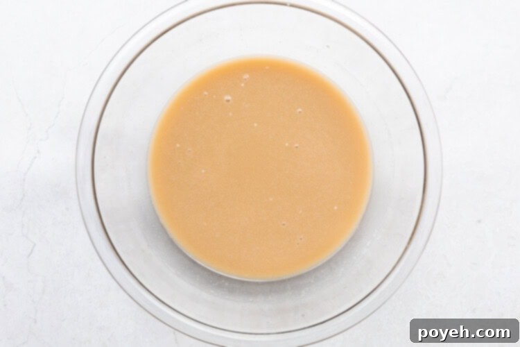 Wet ingredients for pineapple cake batter, including melted vegan butter, non-dairy milk, pineapple juice, and sugars, mixed in a large glass bowl.
