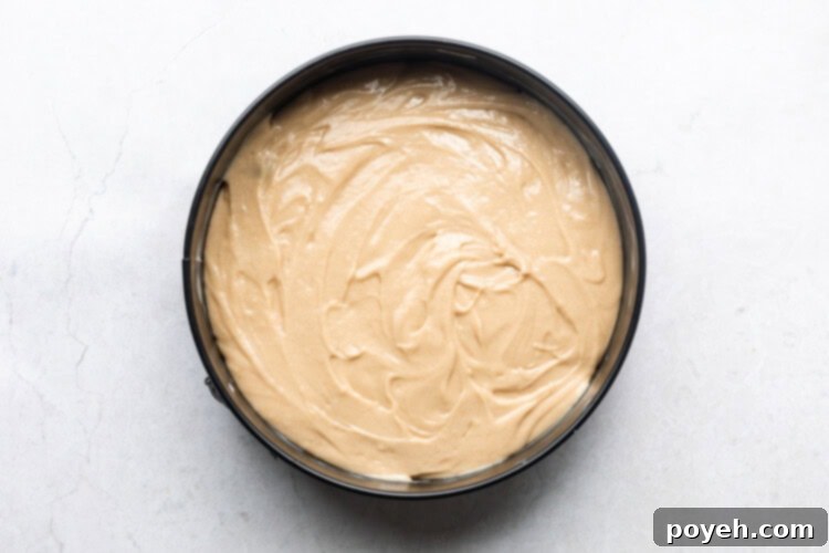 Smooth pineapple cake batter poured over the arranged pineapple slices and cherries in an 8-inch cake pan.