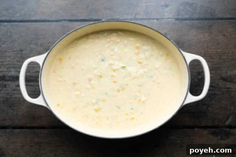 Overhead view of a large soup pot containing a rich, creamy corn soup, simmering gently with both creamed and whole corn kernels.
