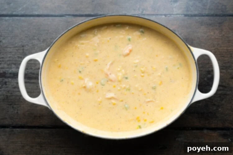 Overhead view of a large soup pot containing shrimp and corn soup with pink, cooked shrimp, seasoned with Old Bay, ready to serve.