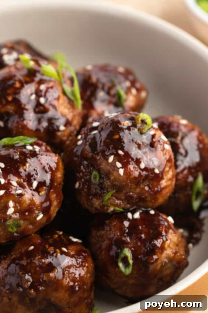 Close-up view of a bowl of Asian turkey meatballs garnished with sesame seeds and green onions.