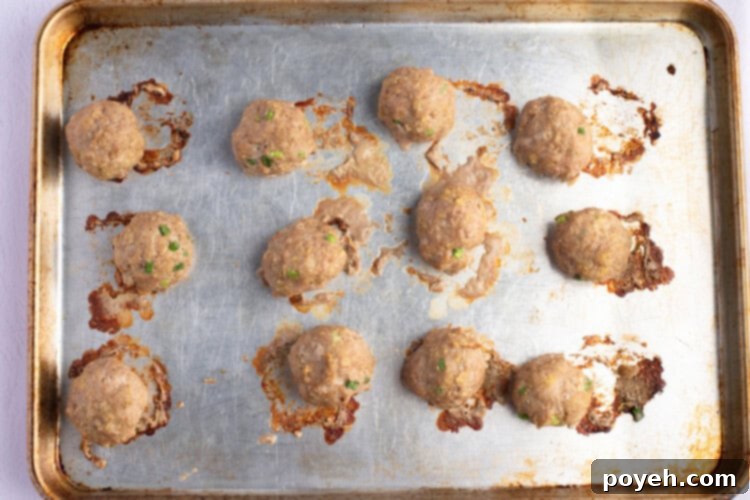 Overhead view of fully-cooked Asian turkey meatballs on a lightly greased baking sheet.