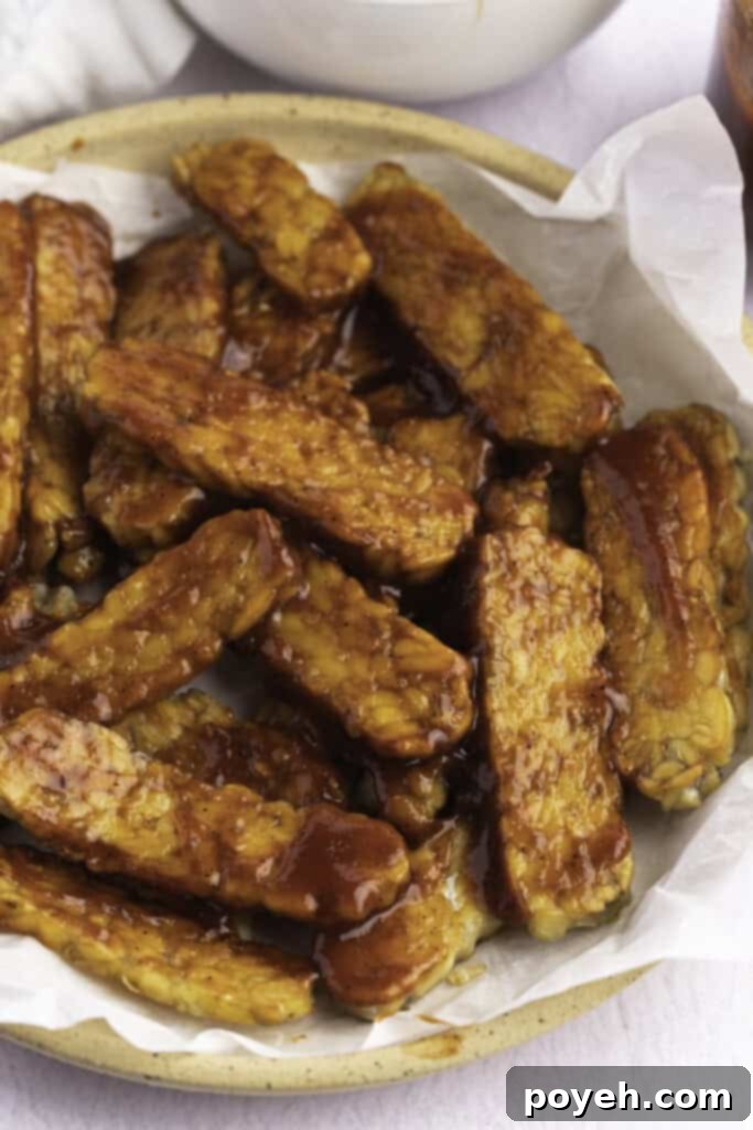 Vegan BBQ sauce on strips of tempeh in a large bowl lined with parchment paper.