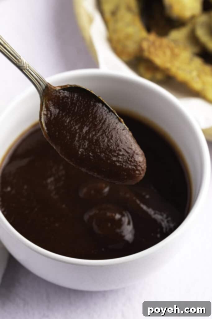 Vegan BBQ sauce in a small white bowl, with a spoon lifting a spoonful of sauce out of the bowl.