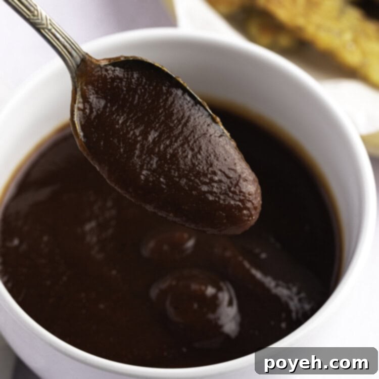 Vegan BBQ sauce in a small white bowl, with a spoon lifting a spoonful of sauce out of the bowl.