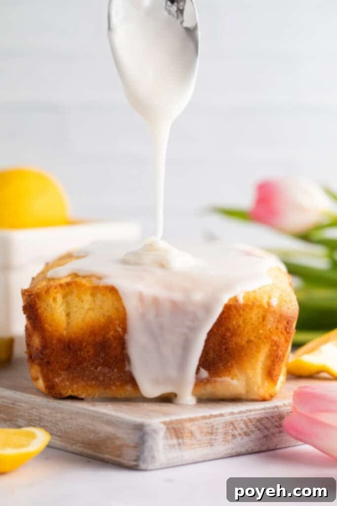 Thick, glossy lemon glaze being artistically poured over a freshly baked gluten-free lemon pound cake loaf, with vibrant tulips providing a cheerful background.