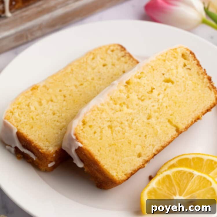 Two generous slices of homemade gluten-free iced lemon pound cake are elegantly arranged on a white plate, accompanied by fresh lemon slices for garnish.