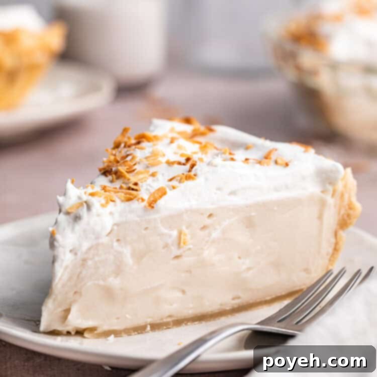 A wedge sliced of vegan coconut cream pie topped with coconut whipped cream and coconut shavings on a neutral plate with a fork.