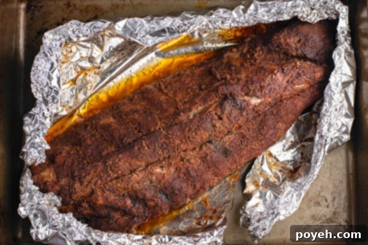A rack of buffalo ribs coated with dry rub and liquid smoke, wrapped in foil on a baking sheet.